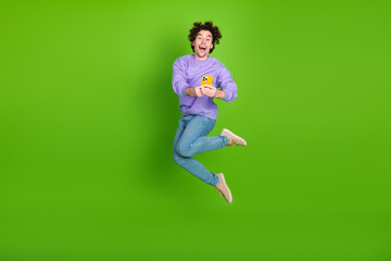 Excited young man wearing trendy purple sweatshirt and blue jeans jumps joyfully holding a yellow...