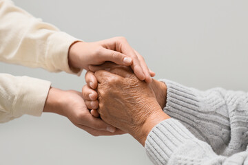 Fototapeta premium Woman holding grandmother's hands on light background