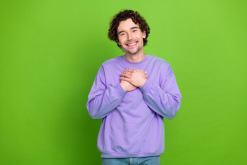 Smiling young man with curly hair in purple sweatshirt standing against green background expressing gratitude