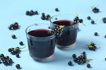 Glasses of fresh black currant juice and berries on blue background