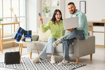 Young couple with credit card and laptop shopping online on sofa at home. Cyber Monday