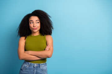 Stylish young woman with a thoughtful expression, folded arms against a blue background, trendy...