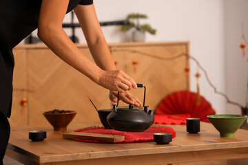 Young Asian woman putting teapot on table in traditional Chinese room