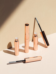 Rose gold eyebrow gel tubes on tan background with shadows 