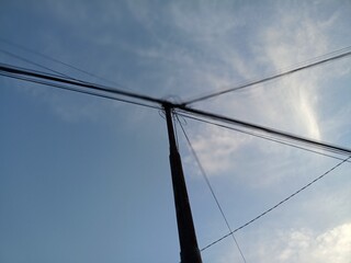 A low-angle view of a utility pole and power lines against a blue sky with wispy clouds.