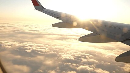 Close-up of airplane wing above cloud sea with glowing sunlight reflecting off metal surface   - Powered by Adobe