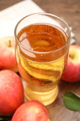 Fresh cider in glass and apples on wooden table, closeup