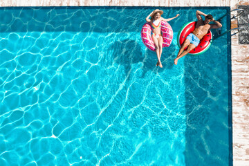 Happy couple with inflatable rings in swimming pool, top view. Summer vacation
