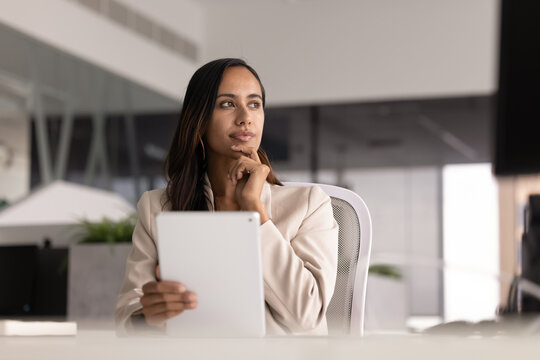 Serious young New Zealander businesswoman holding tablet at office workplace
