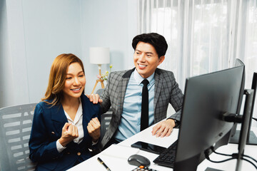 Successful smiling Asian business partners raising fist up together in profitable project job in stock exchange database on pc wearing formal suit at modern home office at side view image. Infobahn.