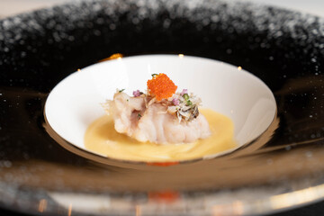 Japanese Fusion Cuisine, Poached White Fish with Creamy Yuzu Sauce, topped with Salmon Roe and Edible Flowers, Fine Dining Appetizer on a Black Ceramic Plate.