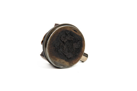 Used engine piston head with carbon deposits isolated on white background, detail of automotive part and wear.
