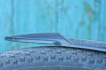 part of a sports bike from a gray tire on the wheel and part of a black plastic fender on the street