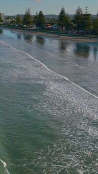 Aerial view of Orewa beach in New Zealand. People are walking and enjoying the beach. The waves are gently rolling in, creating a peaceful scene.