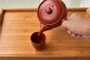 Hand pouring freshly brewed tea from a traditional kyusu teapot into a ceramic cup