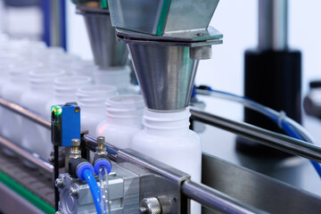 medicine pill capsules are filling in the white plastic bottle on production line machine conveyor at the medical factory.
