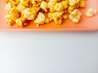 Sweet caramel popcorn on square plate, isolated on white background.