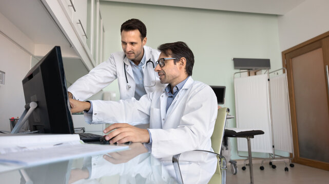 Two interested male doctors analyze digital chart on pc screen