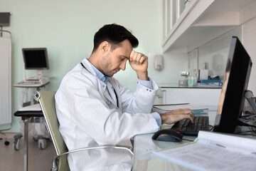 Overworked stressed male doctor sit by computer with closed eyes