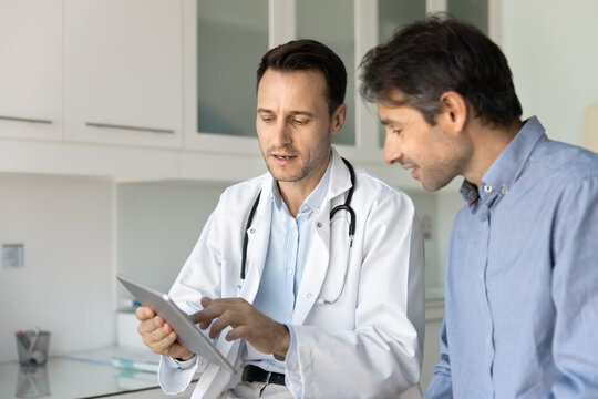 Male doctor and patient talking in clinic office using tablet