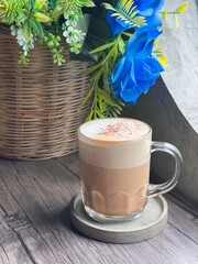 Cozy frothed coffee in a glass mug on a wooden table with floral and basket decor