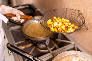 Chef frying potato wedges in restaurant kitchen