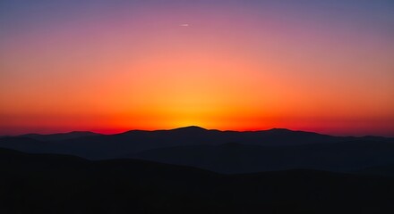 Fototapeta premium Vibrant sunset paints the sky with fiery hues, silhouetting distant mountain ranges.