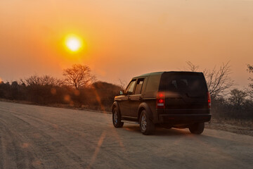 4x4 car driving on a dirt road in the african bush, acacia trees at sunset