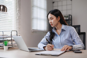Businesswoman working from home office taking notes watching webinar on laptop