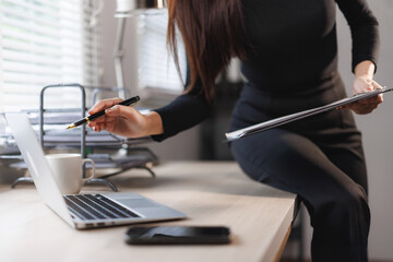 Businesswoman analyzing data on laptop and taking notes in office