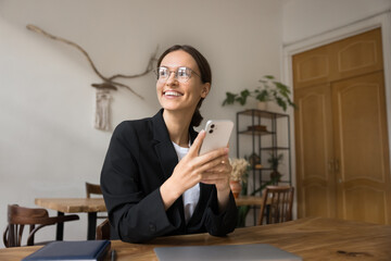 Smiling young businesswoman use smartphone at office desk look aside