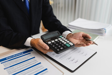 A businessman in a formal suit explains car insurance details, holding a small red car model and...
