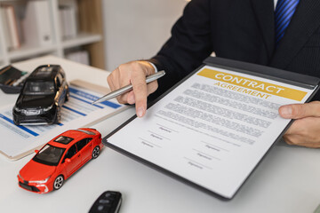 A businessman in a suit is presenting car insurance and contract documents with miniature car...
