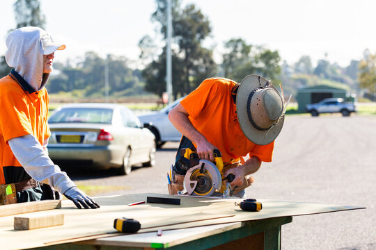 Trade apprentices using cordless circular saw for cutting wood on together during building course
