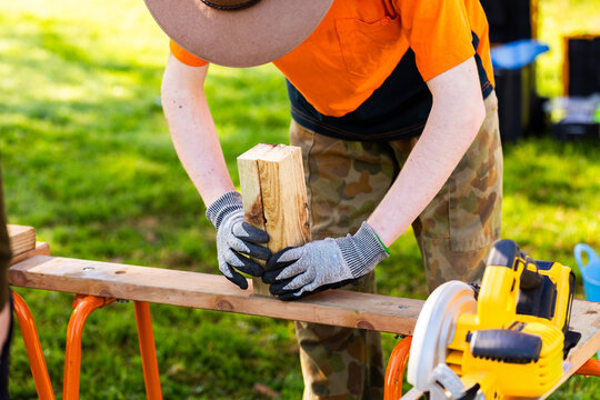 trade apprentice cutting blocks on sawhorse at worksite