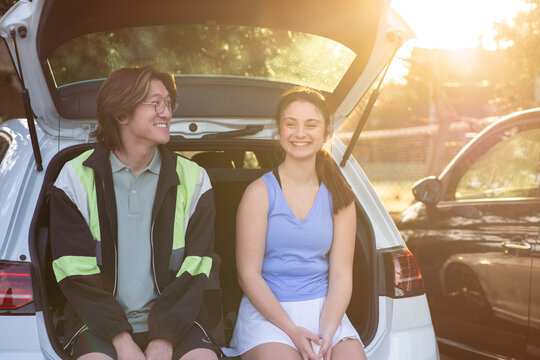 two friends sitting on the bumper of a car after tennis