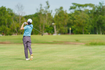 Asian male golfer hitting fairway shot on golf course with sunlight and nature, symbolizing sport, leisure and lifestyle.