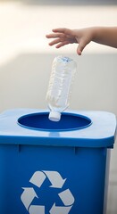 A child's hand disposes of a plastic water bottle into a blue recycling bin, highlighting environmental responsibility.