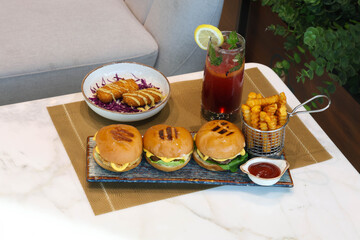 Delicious burgers with fries, nuggets, and a refreshing drink on a table.
