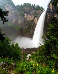 Majestic waterfall cascading down a rocky cliff face, surrounded by lush greenery and wildflowers