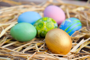 several brightly colored Easter eggs, including blue, pink, green, and a gold one, resting in a nest of straw.