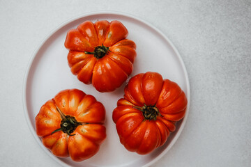 Three ripe red tomatoes with water drops on a white plate with a grey background.