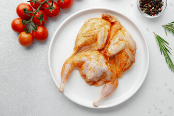 Closeup of marinated raw quail on plate with vine tomatoes and cooking spices