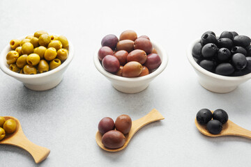 Variety of olives in bowls with wooden spoons on gray background, green olives, black and kalamata olives.