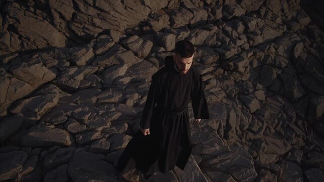 Monk walking over stones. Man in black robe hikes rocky mountain trail in solitude. Religion guides each step in silence. Prayerful walking through forest path shows monk faith and discipline.