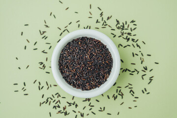 Black rice in white bowl on green background with grains around