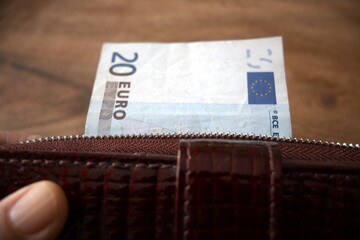 A twenty euro banknote partly visible next to a women’s wallet, close up detail.