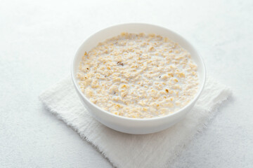Bowl of creamy oatmeal porridge on white towel background