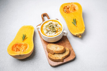 Creamy butternut squash soup with pumpkin seeds and crusty bread served on a wooden board.