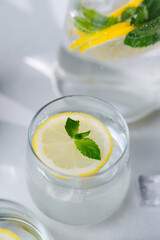 Lemon water with mint leaves and ice served in glass with fresh citrus on light background